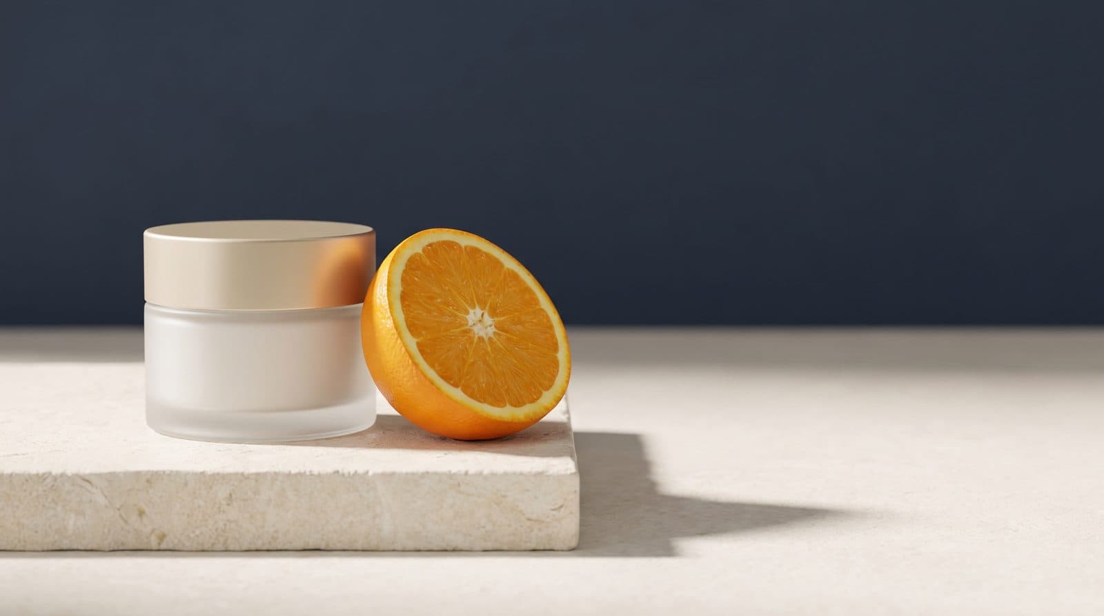 An unlabelled glass jar of cream beside a halved orange on an ivory stone surface in soft morning light